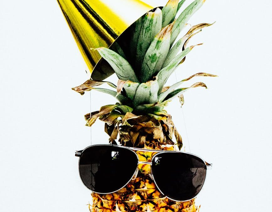 photo of pineapple wearing black aviator style sunglasses and party hat