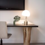 stainless steel base white shade table lamp on brown wooden desk near white painted wall with wall mounted flat screen t v