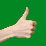close up of a hand showing thumbs up on green background