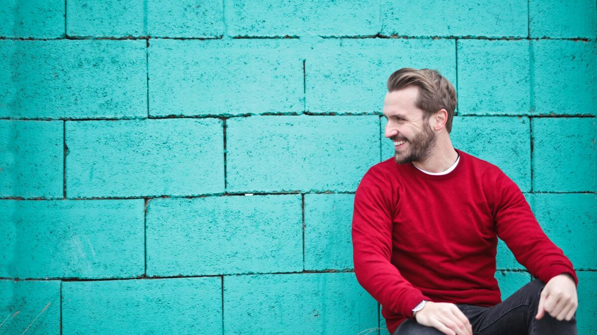 man wearing red sweatshirt and black pants leaning on the wall