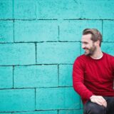 man wearing red sweatshirt and black pants leaning on the wall