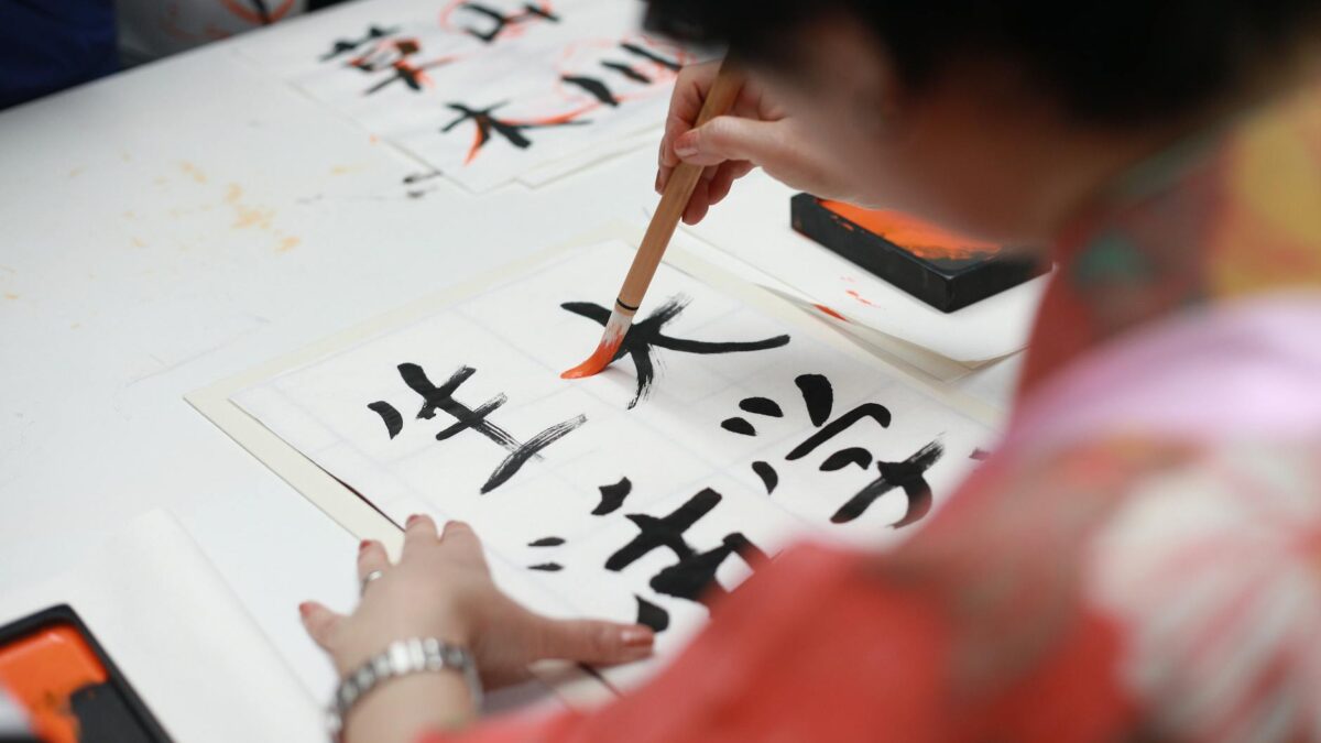 person holding brush drawing kanji script