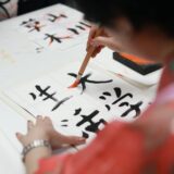 person holding brush drawing kanji script