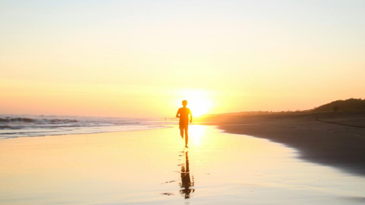 silhouette of boy running in body of water during sunset